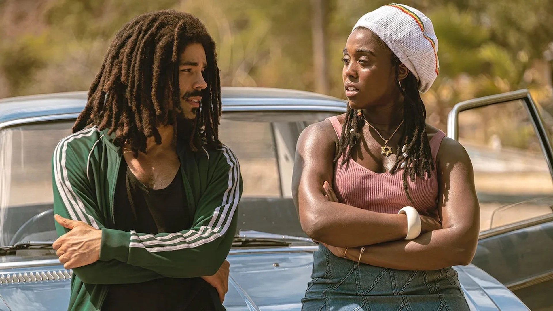 Bob Marley (Kingsley Ben-Adir) and Rita Marley (Lashana Lynch) talking on the hood of a car in 'Bob Marley: One Love'