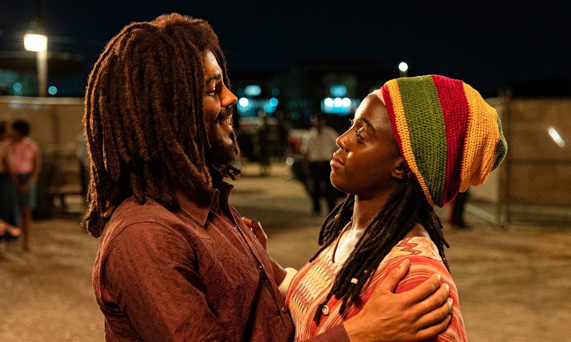 Bob Marley (Kingsley Ben-Adir) and Rita Marley (Lashana Lynch) hugging in a parking lot in 'Bob Marley: One Love' 