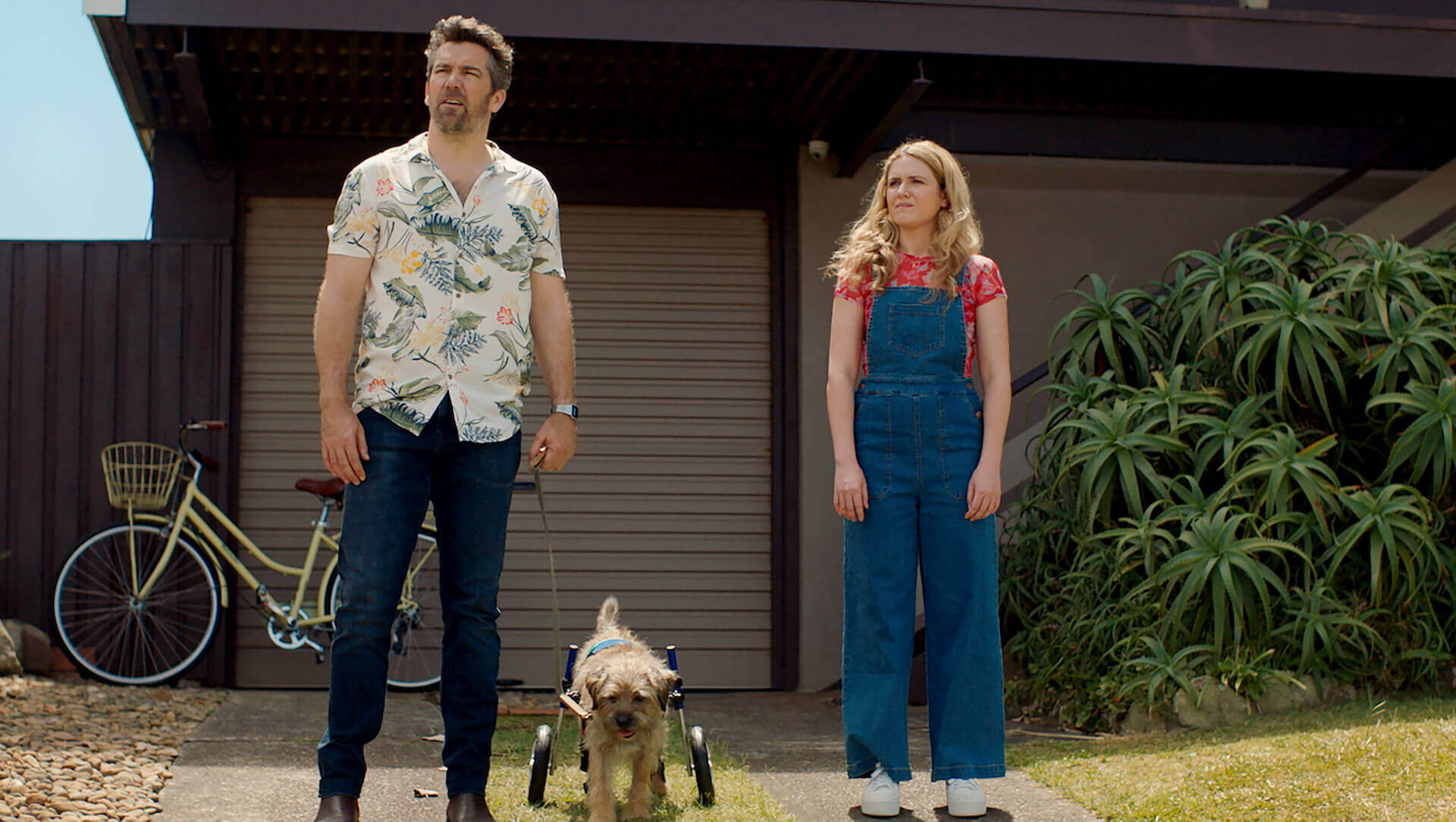 Patrick Brammall and Harriet Dyer standing with a dog infront of a house in 'Colin From Accounts'