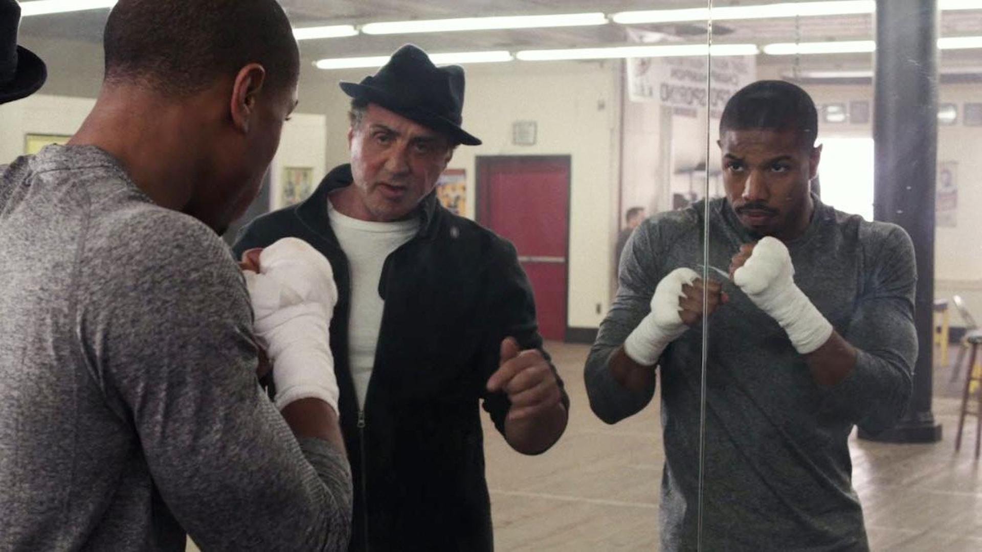 Donnie Creed (Michael B. Jordan) looking into a practice mirror while Rocky (Sylvester Stallone) coaches him in 'Creed' (2015)