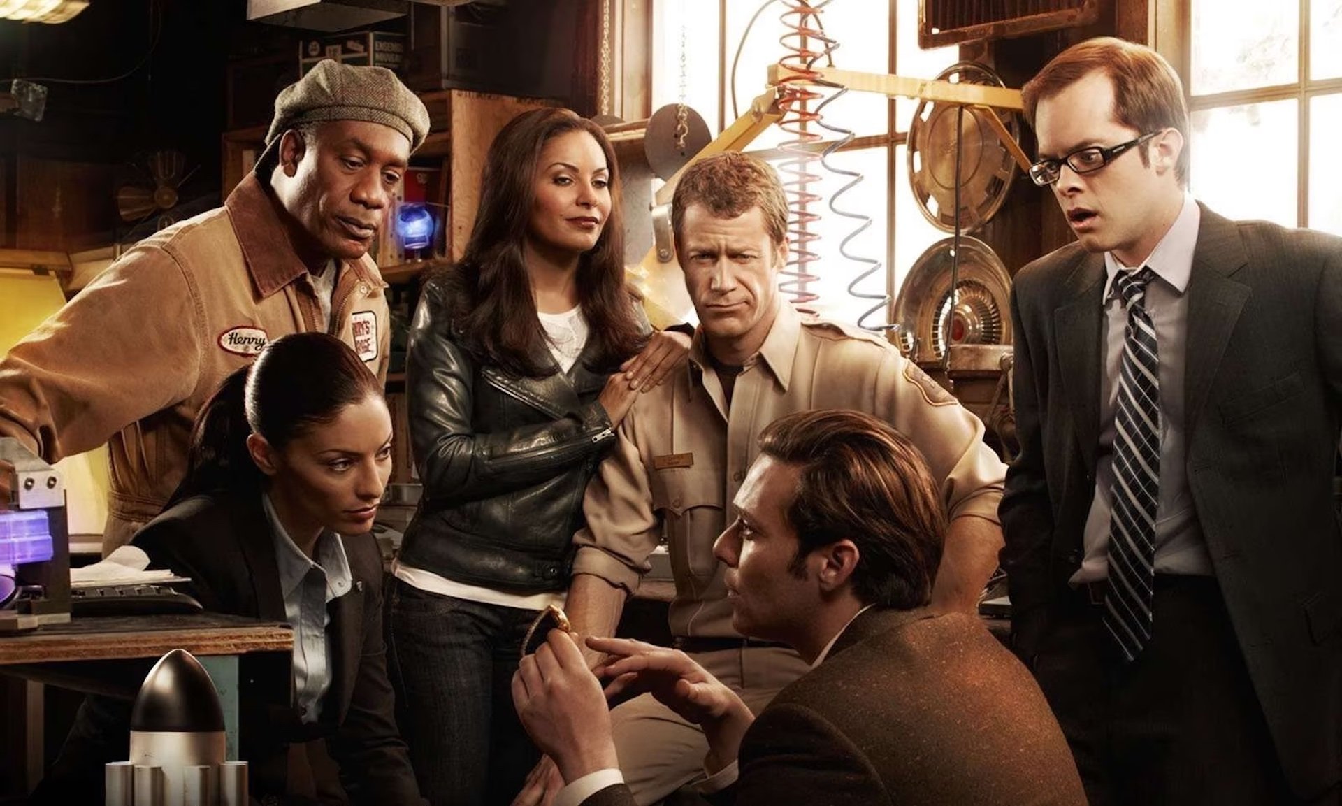 The cast of 'Eureka' looking at a watch in a promo photo; Finding Your Lane With 'The Flash' Showrunner Eric Wallace
