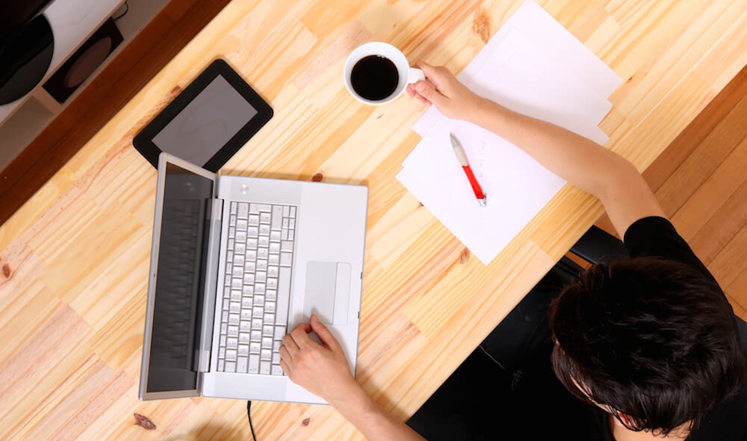 A man with black hair typing on her laptop while holding a cup of coffee, 5 Editing Hacks for Screenwriters