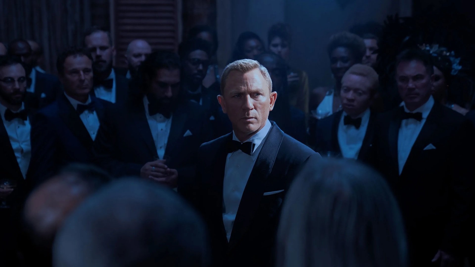 James Bond (Daniel Craig) standing in a circle of men in suits in 'No Time to Die'