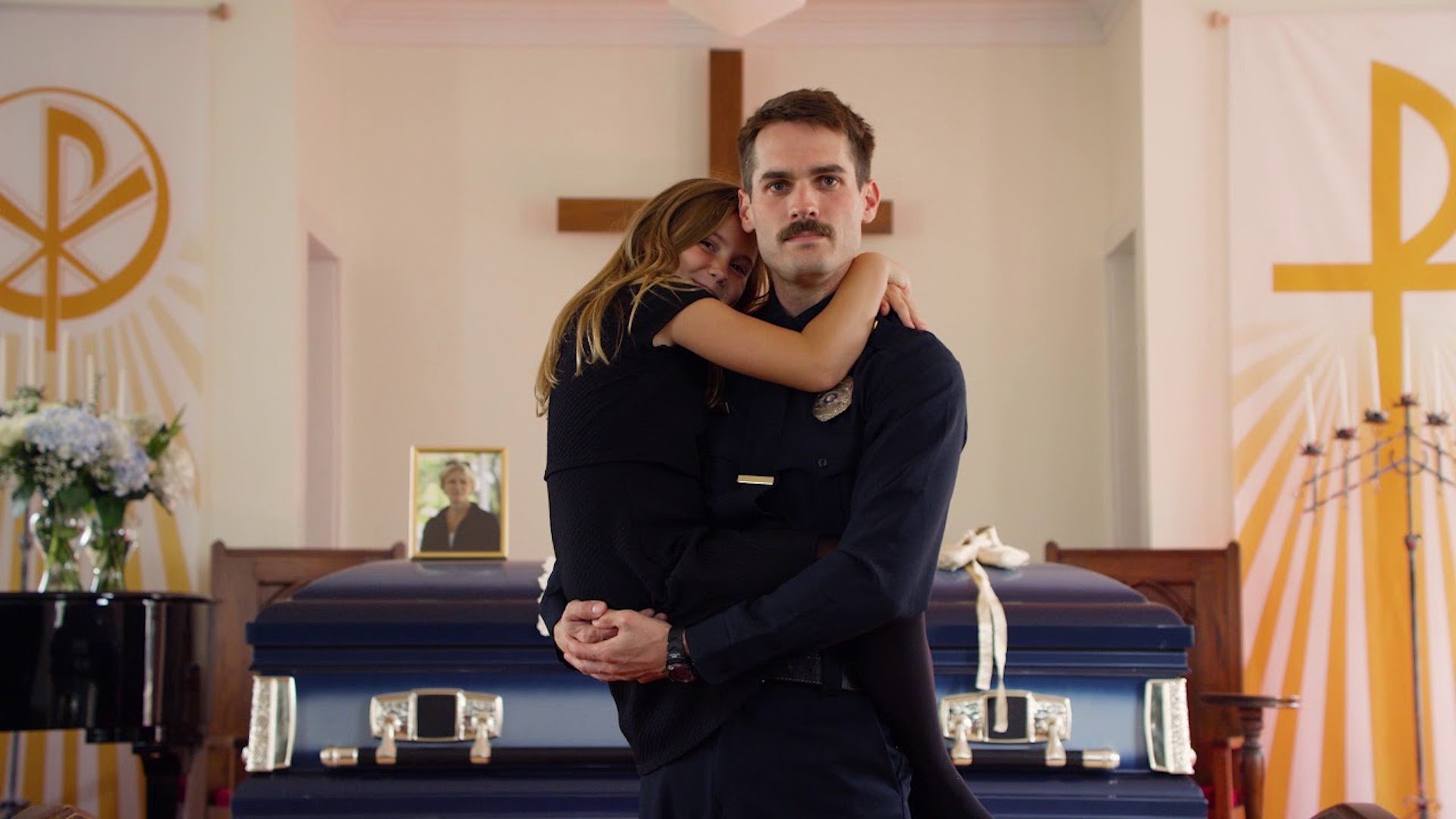 A police officer holding a young girl at a funeral house in 'Thunder Road'