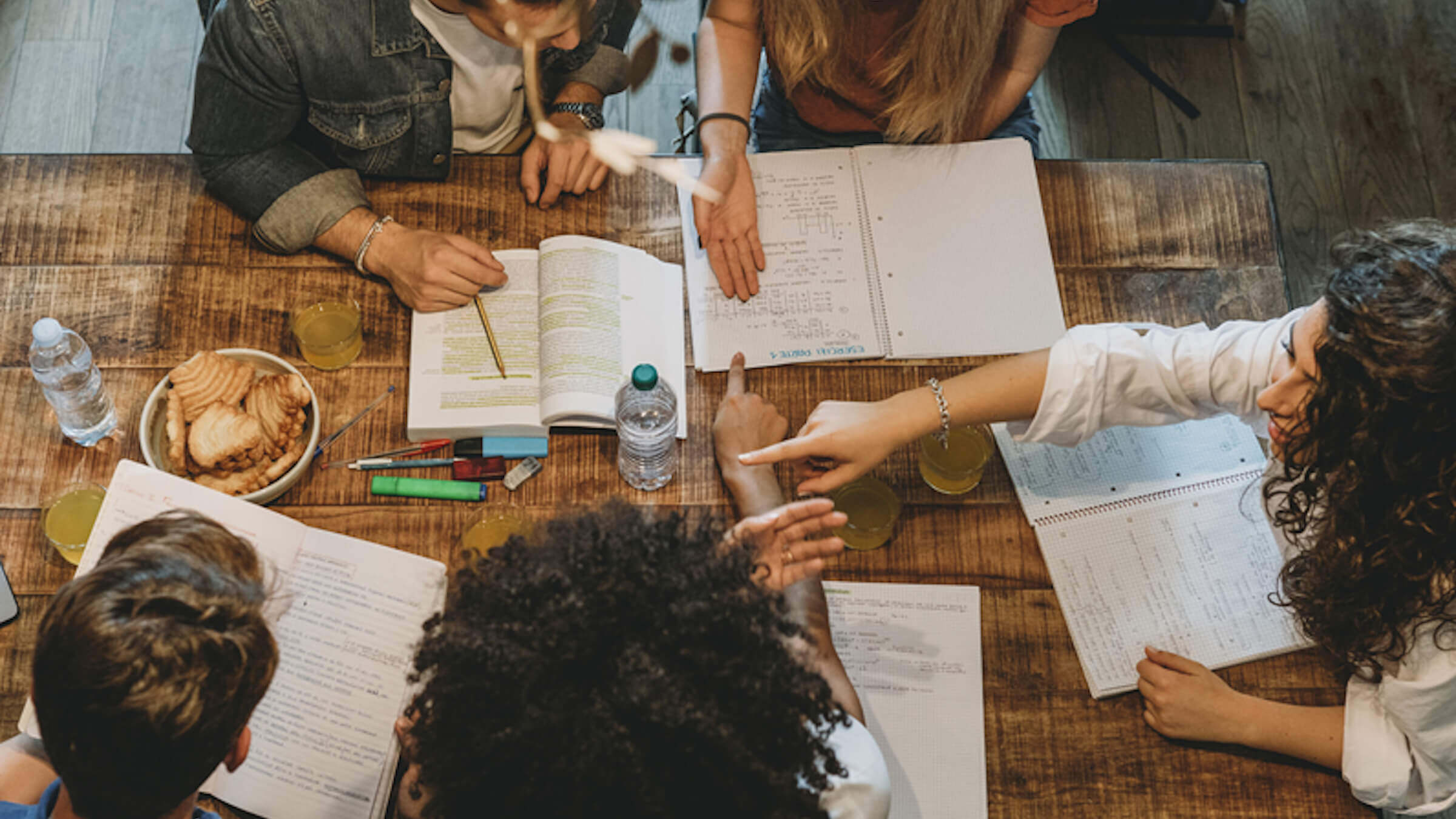 People talking over notebooks on a wooden table, Writers' Room Etiquette for Screenwriters